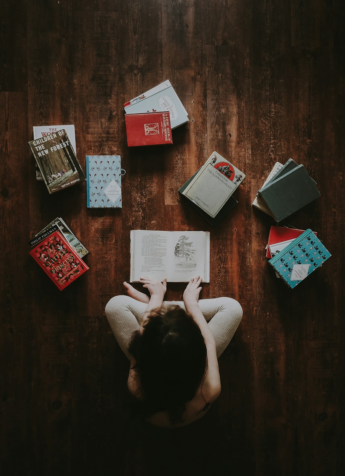 Person sitting on the floor surrounded by a pile of books to work through