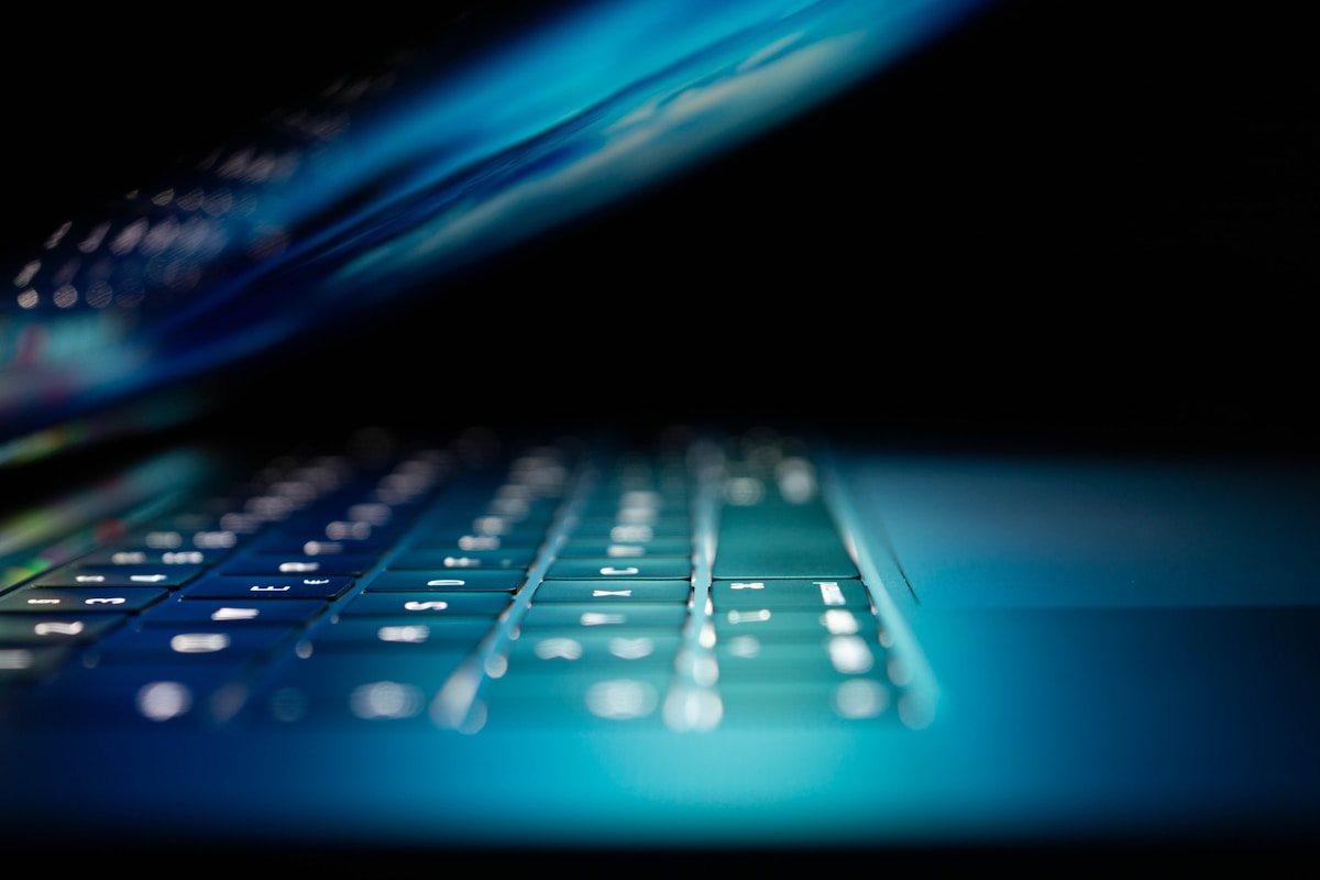 Laptop keyboard glowing blue in a dark room, representing cybersecurity work