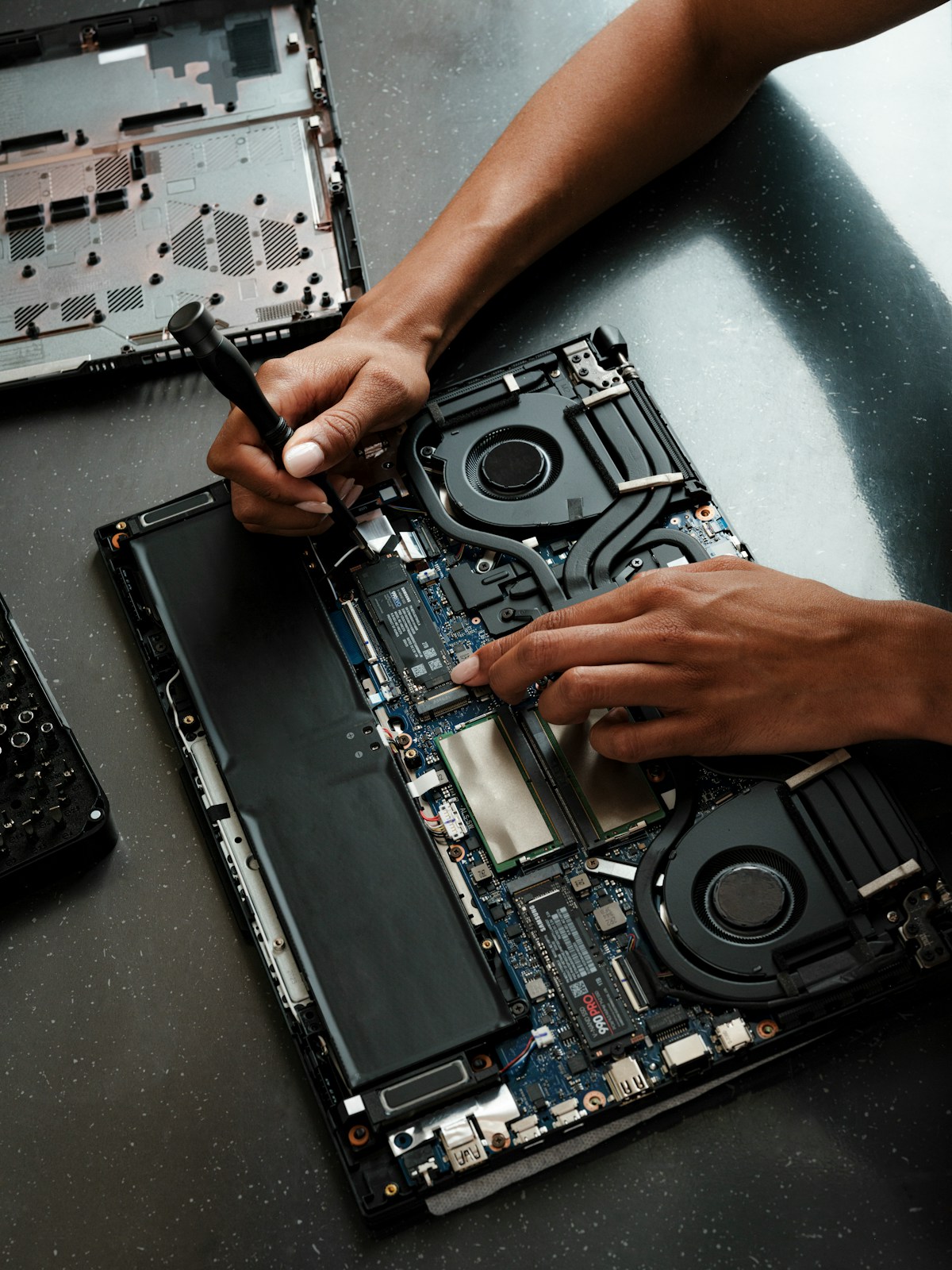 Hands using a screwdriver to repair the internal components of a laptop