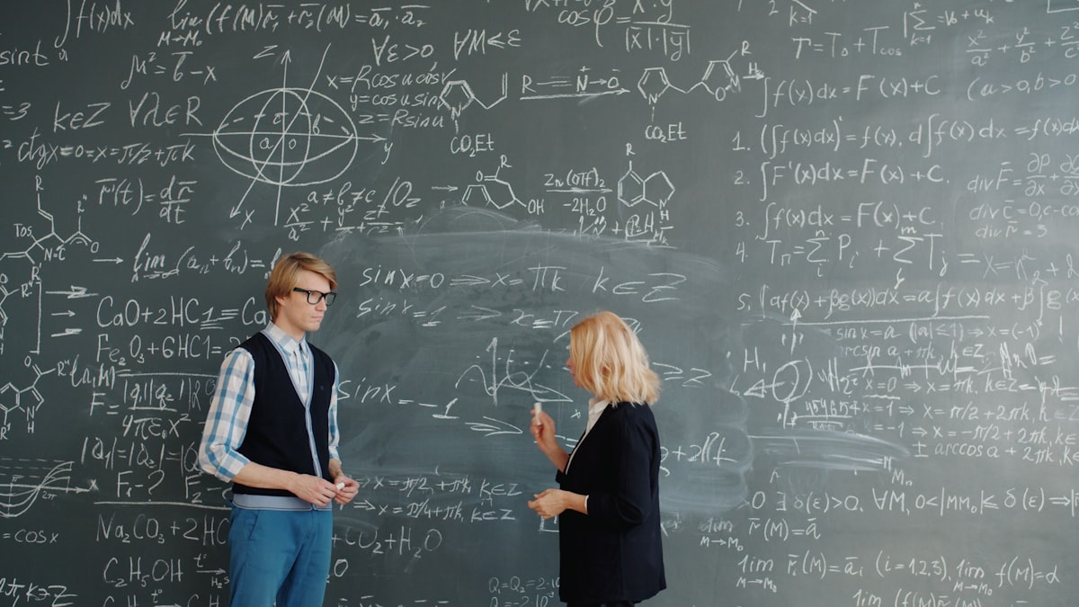 Two students discussing math formulas on a blackboard for STEM note-taking