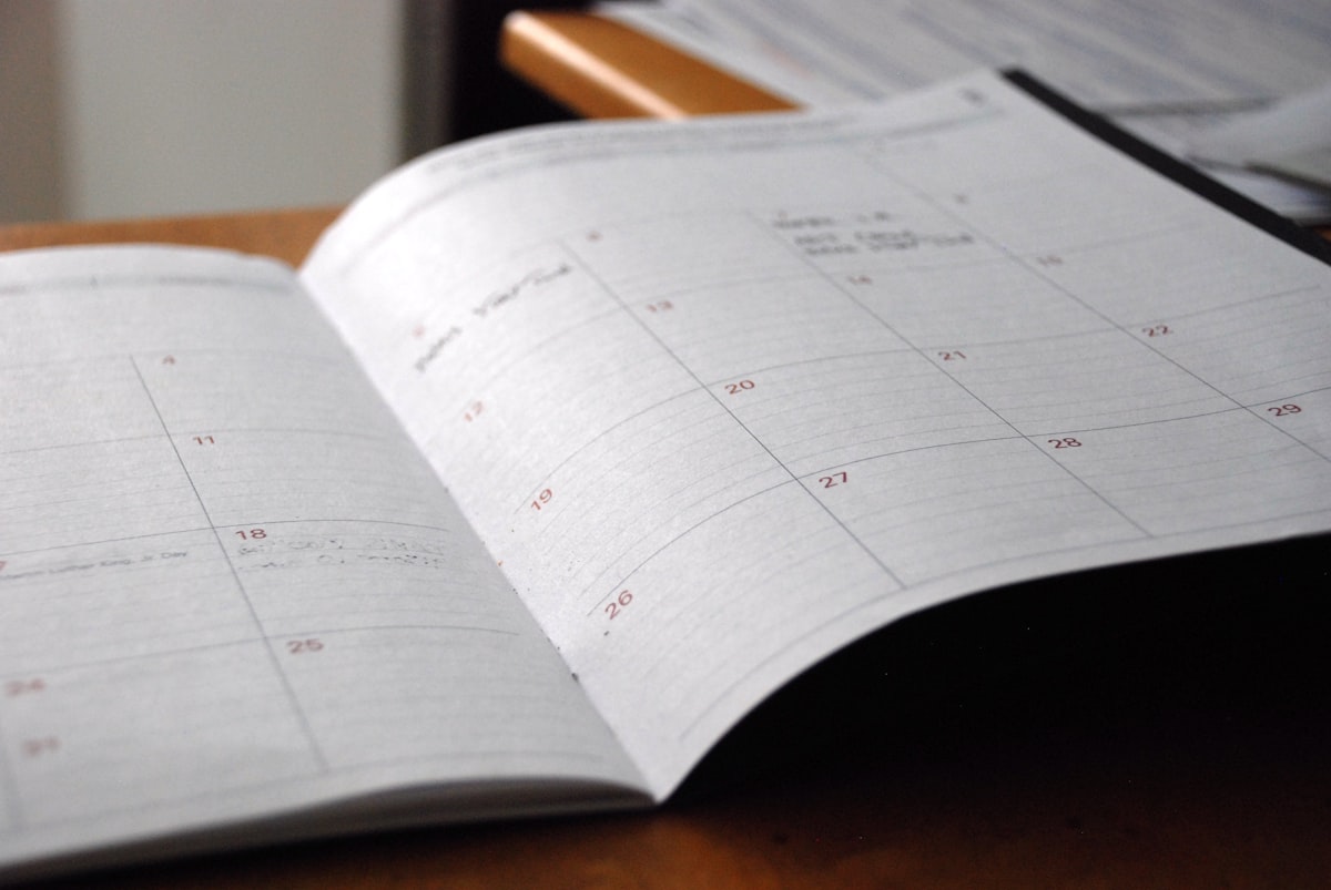 Open monthly planner on a wooden desk with pen and coffee cup