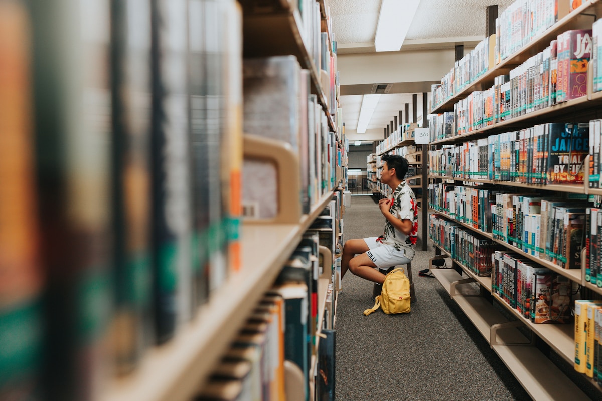 College student sitting among the bookshelves of a university library