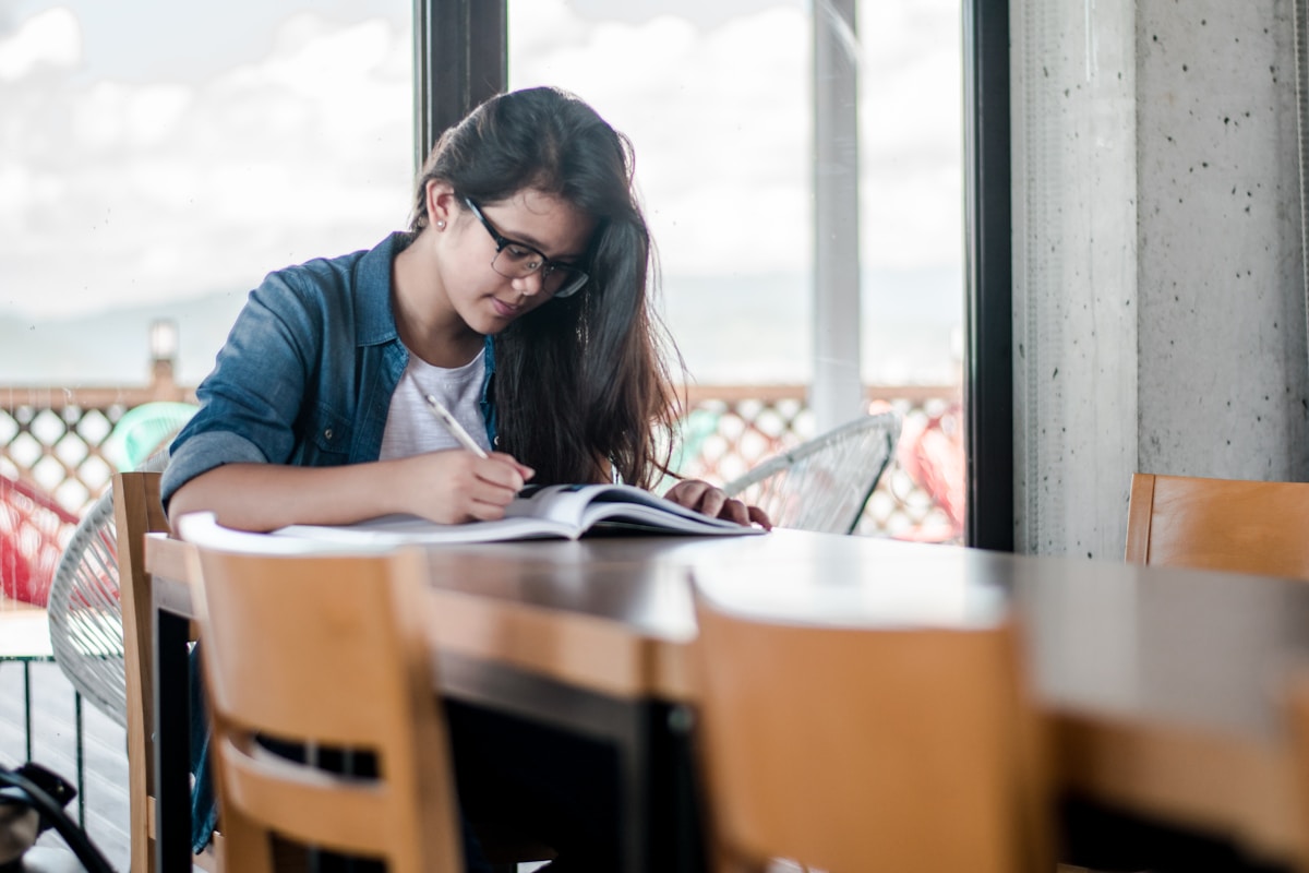 Student smiling while studying with a notebook at a sunlit desk