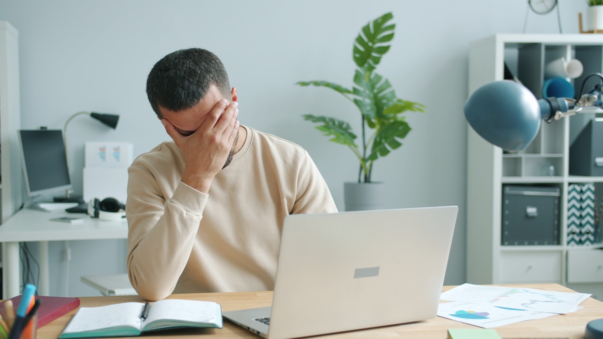 Stressed person holding their head in front of a laptop at a desk
