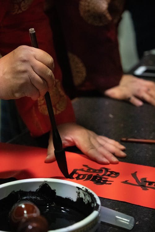 Person practicing Chinese calligraphy with brush and ink