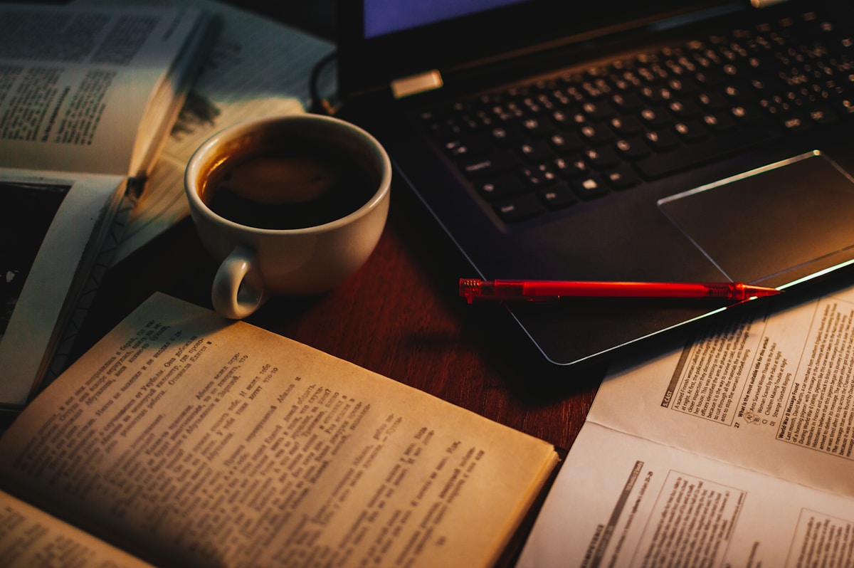 Cup of coffee next to an open book and laptop during a late night study session